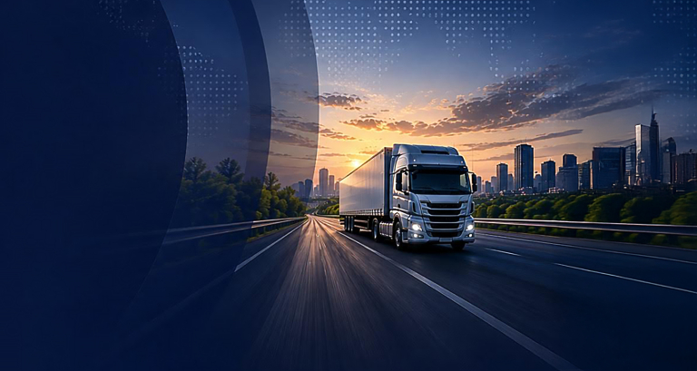 Silver semi-truck driving on a highway toward a distant city skyline at sunset